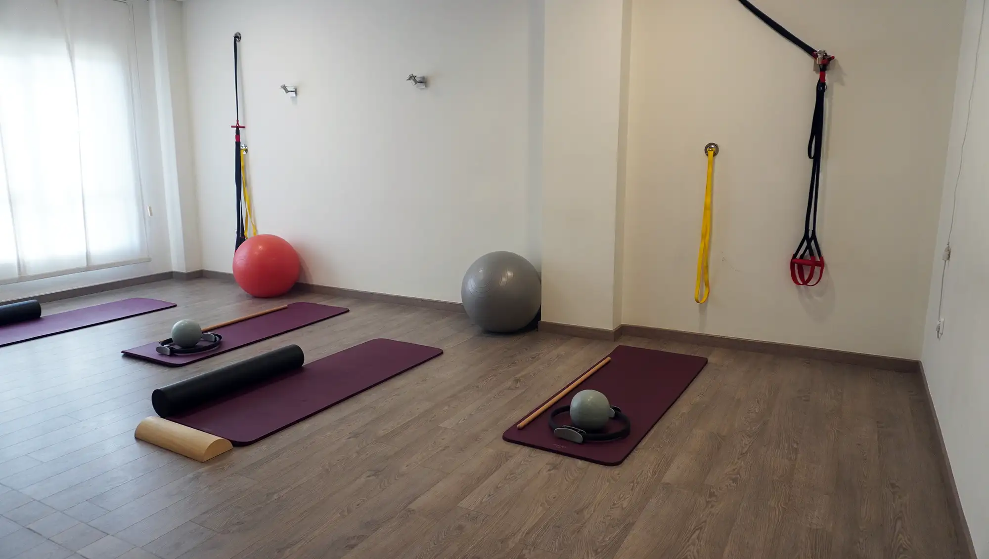 Vista general de la sala de pilates con colchonetas burdeos y material de entrenamiento distribuido.