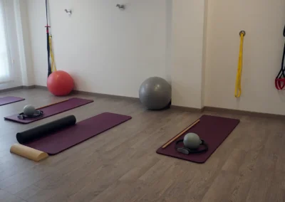 Primer plano de colchoneta con aro de pilates, palo de madera y rodillos de espuma sobre suelo de madera.