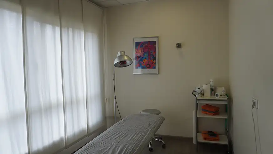 Sala de tratamiento con camilla, lámpara terapéutica y equipamiento para fisioterapia.