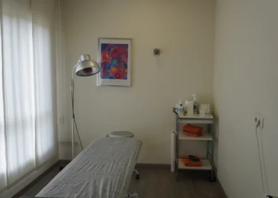 Sala de tratamiento con camilla, lámpara infrarroja y carro con material clínico.