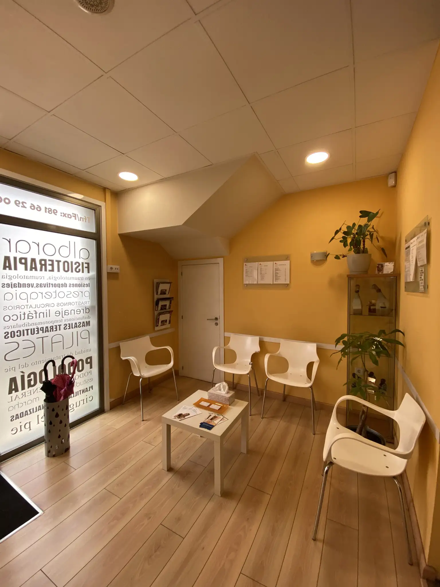Recepción y sala de espera con sillas blancas y mesa central con folletos.
