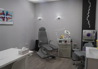 Consulta de podología con sillón clínico, instrumental especializado y zona de lavado. Sillón podológico en consulta equipada con lámpara de aumento y material clínico. Gabinete de podología con equipamiento sanitario y zona de trabajo del especialista.