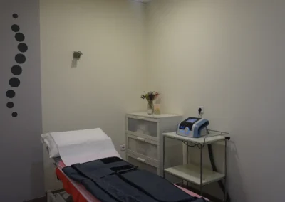 Consulta de fisioterapia con camilla, equipo de presoterapia y decoración minimalista.