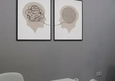 Consulta de psicología con mesa blanca, sillas, caja de pañuelos y láminas decorativas en la pared.