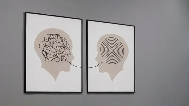 Consulta de psicología con mesa blanca, sillas, caja de pañuelos y láminas decorativas en la pared.